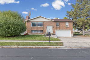 Split foyer home featuring concrete driveway, brick siding, a chimney, and an attached garage