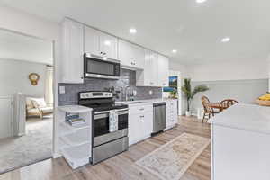 Kitchen with appliances with stainless steel finishes, white cabinets, light stone countertops, light wood-type flooring, and recessed lighting