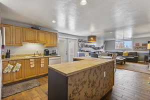 Kitchen featuring dark wood-style floors, open floor plan, brown cabinets, a kitchen island, and a textured ceiling