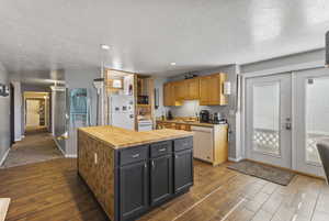 Kitchen featuring butcher block counters, white appliances, dark wood-style flooring, a textured ceiling, and a kitchen island
