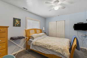 Bedroom with a closet, carpet floors, ceiling fan, and a textured ceiling