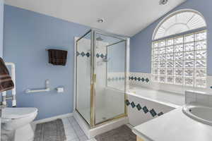 Full bathroom with a stall shower, a bath, vanity, light tile patterned floors, and vaulted ceiling