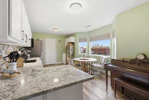 Kitchen featuring white cabinets, light granite countertops, light wood-type flooring, backsplash, and a peninsula