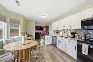 Kitchen with appliances with stainless steel finishes, backsplash, white cabinets, light wood-type flooring, and light granite counter tops