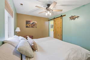 Primary bedroom with a barn door to bathroom and a ceiling fan