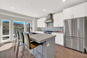 Kitchen featuring stainless steel appliances, decorative backsplash, light wood-type flooring, wall chimney exhaust hood, and a center island with sink