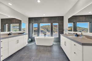 Bathroom with tile walls, two vanities, a freestanding tub, healthy amount of natural light, and recessed lighting
