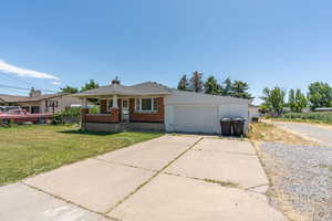 Bungalow-style home featuring brick siding, a front lawn, a chimney, driveway, and covered porch