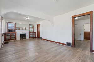Unfurnished living room featuring arched walkways, light wood-style flooring, and a brick fireplace