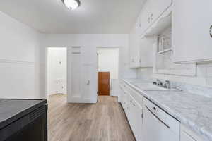 Kitchen featuring light wood-style floors, light countertops, white cabinets, and white dishwasher