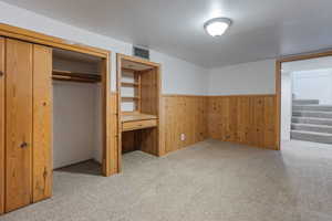 Unfurnished bedroom with light carpet, a closet, wooden walls, and built in study area