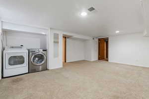 Laundry area featuring light colored carpet, washer and clothes dryer, and a textured ceiling