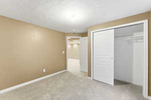 Unfurnished bedroom featuring light colored carpet, a closet, and a textured ceiling