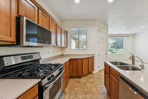 Kitchen featuring appliances with stainless steel finishes, brown cabinets, light stone counters, recessed lighting, and light tile patterned flooring