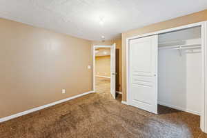 Unfurnished bedroom featuring dark colored carpet, a closet, and a textured ceiling