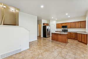 Kitchen featuring brown cabinets, appliances with stainless steel finishes, recessed lighting, an island with sink, and light tile patterned flooring