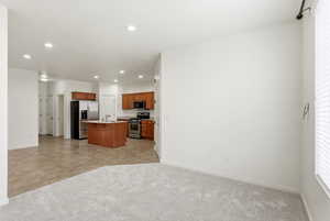 Kitchen with open floor plan, an island with sink, light colored carpet, light countertops, and wood finish cabinetry