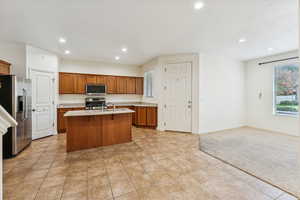 Kitchen featuring appliances with stainless steel finishes, brown cabinets, an island with sink, recessed lighting, and open floor plan