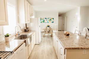 Kitchen featuring light wood-style floors, white appliances, a kitchen island, light stone countertops, and recessed lighting