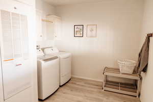 Washroom featuring a heating unit, light wood-style floors, washer and clothes dryer, and cabinet space