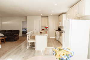 Kitchen featuring white appliances, light wood-style floors, recessed lighting, a breakfast bar area, and open floor plan