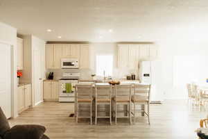 Kitchen with white appliances, a breakfast bar, a kitchen island, light wood finished floors, and recessed lighting