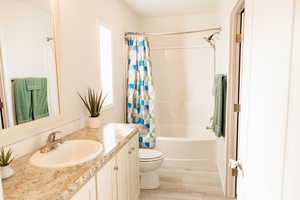 Full bath featuring vanity, shower / bathtub combination with curtain, and light wood finished floors
