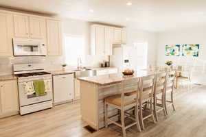 Kitchen featuring white appliances, a center island, healthy amount of natural light, a breakfast bar, and recessed lighting