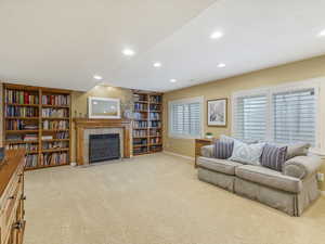 Additional basement family room with recessed lighting, light colored carpet, a fireplace with flush hearth, and built in shelves