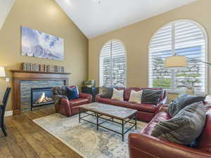 Family room featuring healthy amount of natural light, wood finished floors, a stone fireplace, and high vaulted ceiling