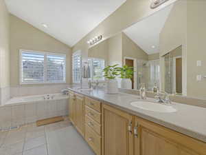 Master bathroom with double vanity, light tile patterned floors, a glass shower, a vetted bathtub and high vaulted ceiling