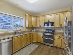 Kitchen with stainless steel appliances, wood finished floors, light stone counters, and light brown cabinetry