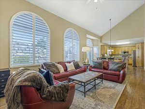 Open concept family room area with light wood-type flooring, high vaulted ceiling, ceiling fan, and a chandelier