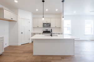 Kitchen with light wood-style floors, stainless steel appliances, a center island with sink, backsplash, and white cabinets