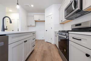 Kitchen featuring stainless steel appliances, white cabinetry, light wood-type flooring, decorative backsplash, and hanging light fixtures
