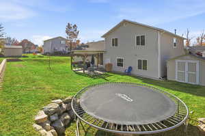 Back of property featuring a storage shed, a patio area, a yard, and a trampoline