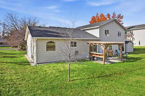 Back of property with a pergola, a yard, roof with shingles, and a patio area