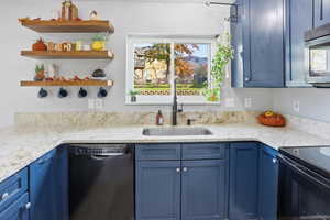 Kitchen with blue cabinets, light stone counters, black appliances, and open shelves