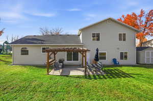 Back of house with a pergola, a storage unit, a lawn, a patio area, and roof with shingles