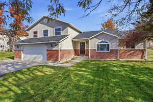 View of front of property with a front yard, an attached garage, driveway, brick siding, and stucco siding