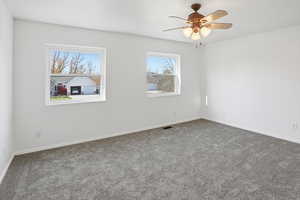 Primary bedroom featuring brand new carpet and paint, two large windows and a ceiling fan
