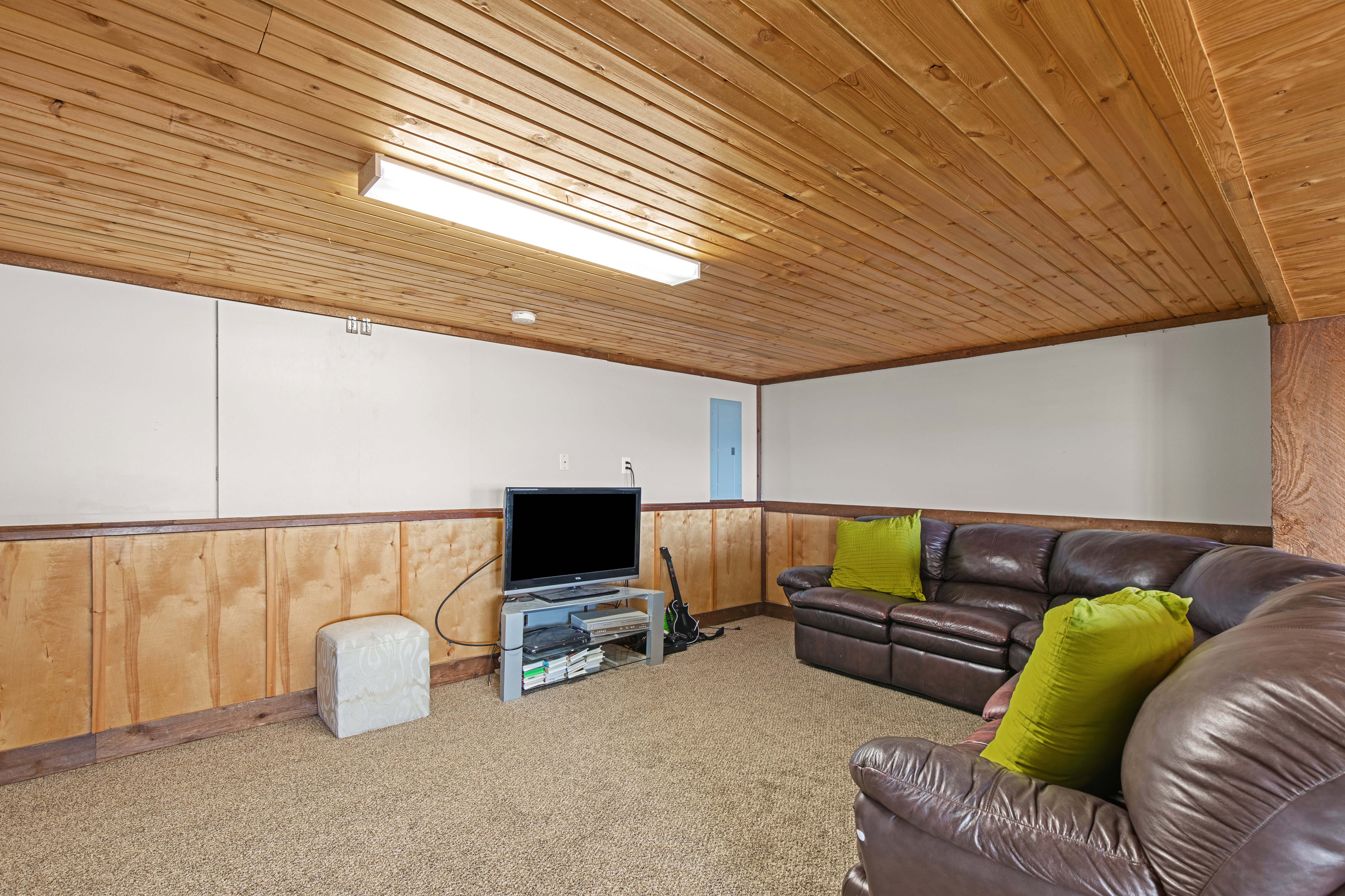 Living area with carpet flooring, wooden walls, wood ceiling, and wainscoting