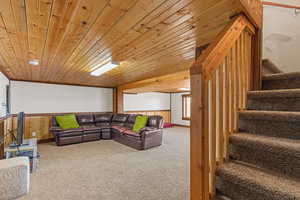 Carpeted living room with stairs, wood walls, and wooden ceiling