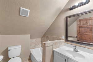 Full bathroom featuring a textured ceiling, a garden tub, vanity, lofted ceiling, and tile walls
