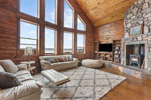 Living room featuring high vaulted ceiling, hardwood / wood-style flooring, wood walls, a wood stove, and plenty of natural light