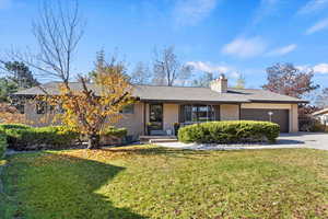 Ranch-style house featuring a front lawn, a porch, brick siding, a chimney, and a garage