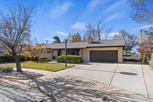 Ranch-style house featuring concrete driveway, a chimney, brick siding, a garage, and roof with shingles