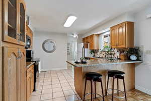 Kitchen featuring electric range, a breakfast bar, glass insert cabinets, decorative backsplash, and a peninsula