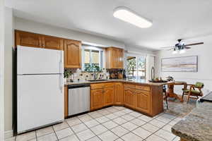 Kitchen featuring brown cabinetry, freestanding refrigerator, a peninsula, dark stone countertops, and backsplash