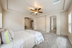Carpeted bedroom with a tray ceiling, arched walkways, and a ceiling fan
